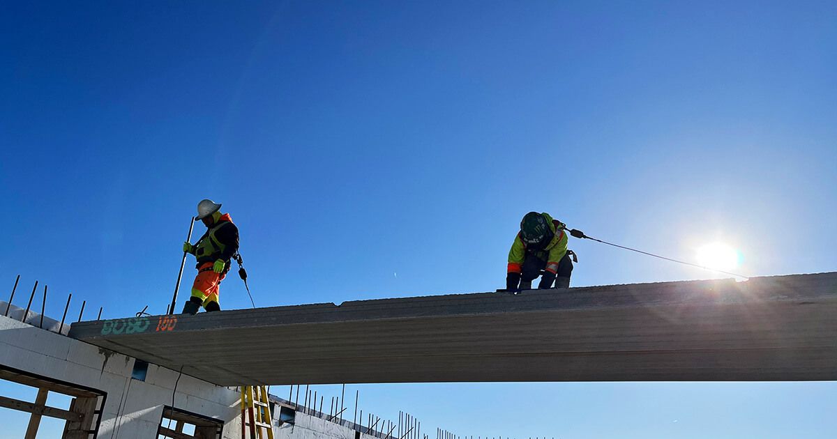 Two construction workers on top of a hollowcore slab during floor system construction.